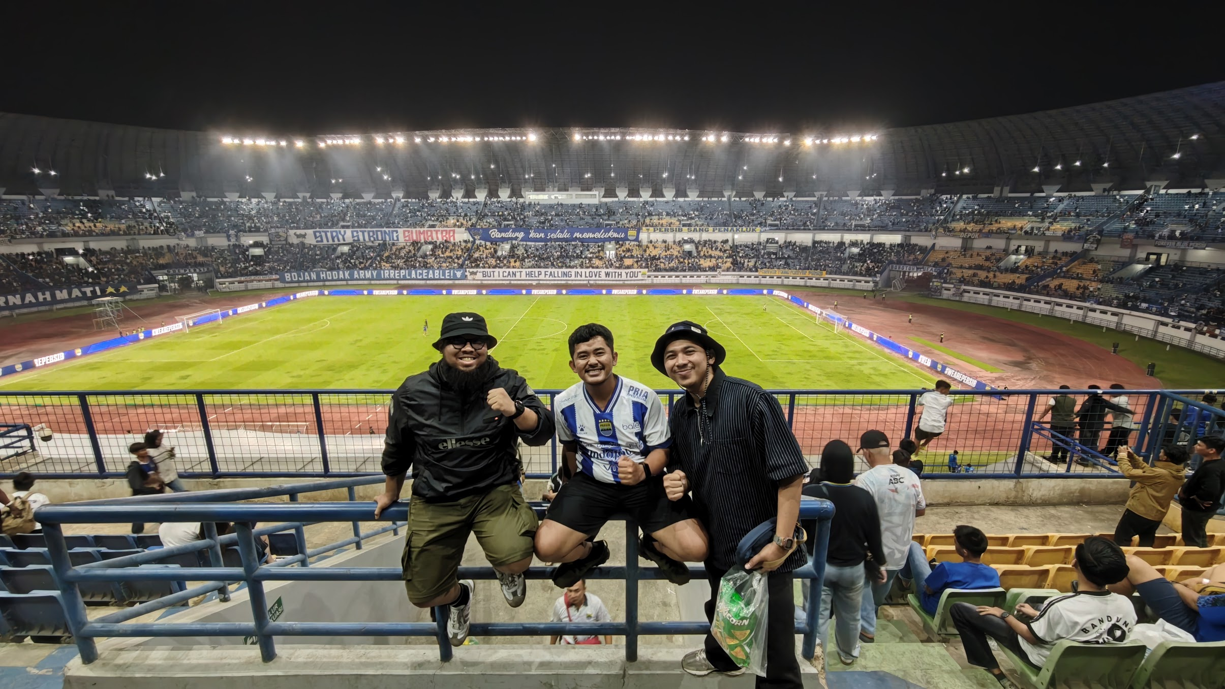 Tegar and two friends at a football match in a stadium.